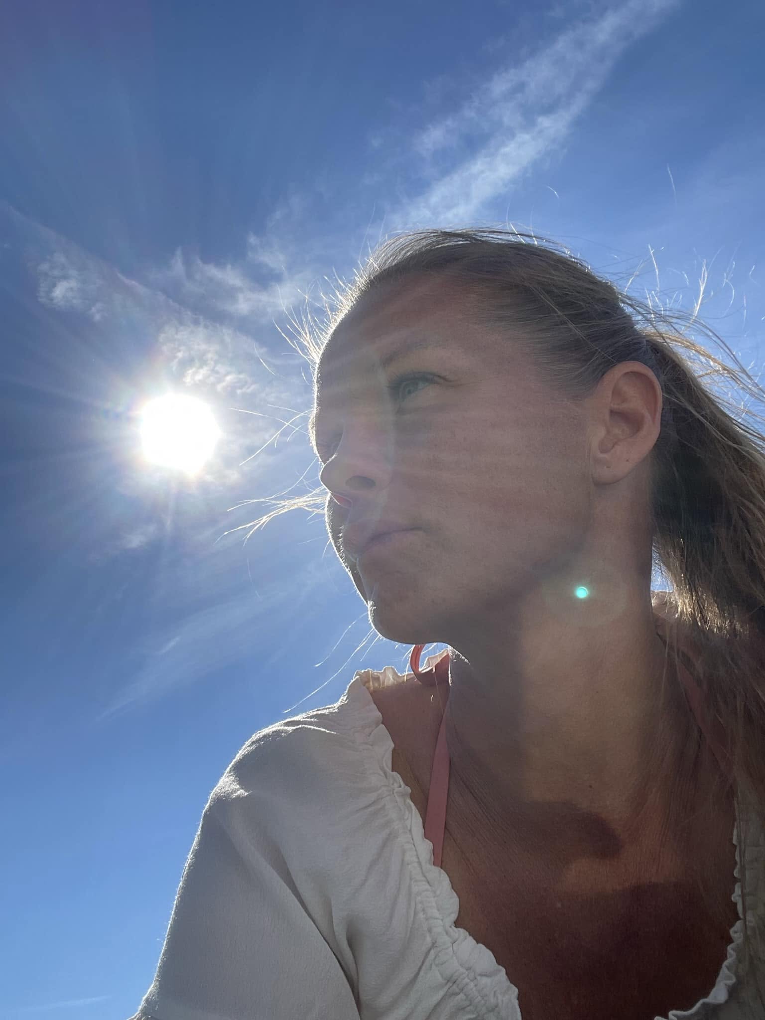 Carine Schackt i profil mot en klar blå himmel med sola som skinner