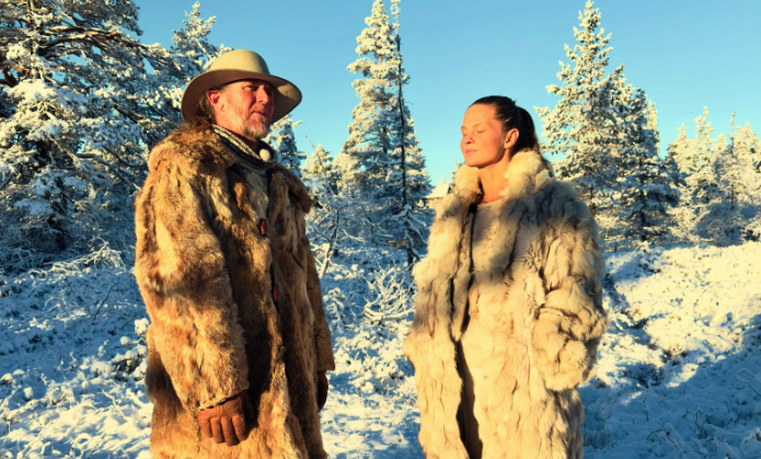 Christian og Carine i pelskåper i en snødekt skog i vintersol
